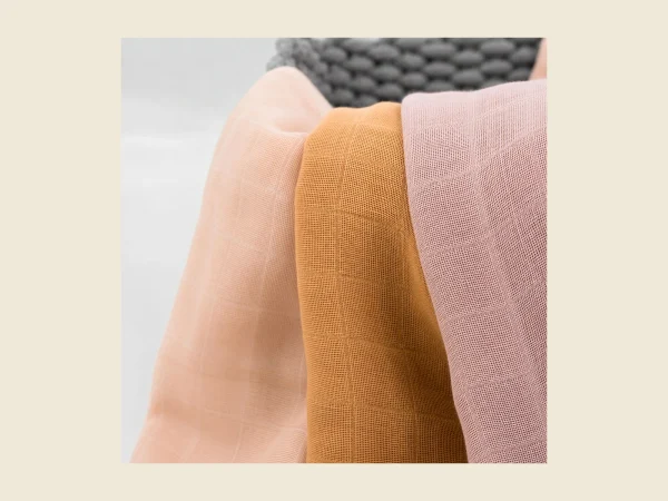 Baby muslin squares folded in soft pastel tones showing the double gauze texture
