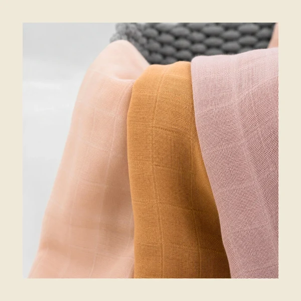 Baby muslin squares folded in soft pastel tones showing the double gauze texture