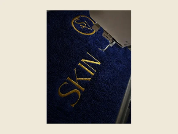 Navy towel with gold embroidered lettering shown close up on the embroidery machine