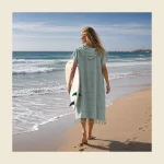 Hammam towel poncho in soft mint flat-woven peshtemal cloth worn on the beach with a surfboard