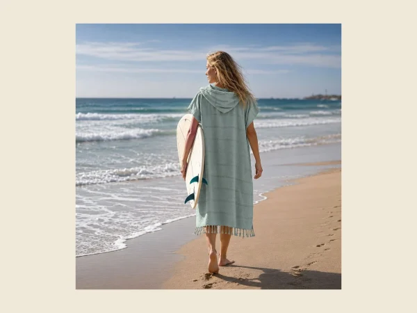 Hammam towel poncho in soft mint flat-woven peshtemal cloth worn on the beach with a surfboard
