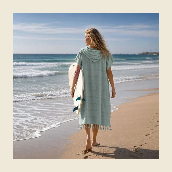 Hammam towel poncho in soft mint flat-woven peshtemal cloth worn on the beach with a surfboard