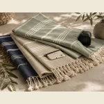 Hidden pocket peshtemals in sage and navy folded with a phone and sunglasses alongside — zippered pocket