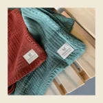 Muslin blankets in rust and teal with a crinkled double-gauze texture and MONNEVA labels