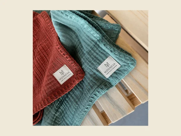 Muslin blankets in rust and teal with a crinkled double-gauze texture and MONNEVA labels