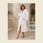 White hooded spa bathrobe with MONNEVA embroidery beside a wellness pool