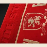 Red sports club towel with a jacquard-woven club crest shown close up