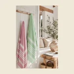 Terry-backed peshtemals in rose and green stripe hanging on a wall rail — flat-woven face with absorbent terry reverse