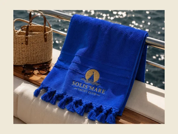 Blue yacht club towel with a gold embroidered emblem and knotted fringe on a boat deck