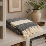 Folded black and white diamond-patterned hammam towel with cream hand-knotted tassels on a plaster console