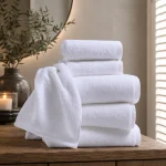 Stack of white terry hotel towels in bath sheet, bath, hand and face sizes on a wooden console with olive branch — MONNEVA