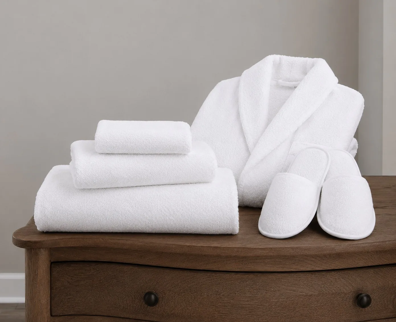 Luxury Hotel Towels — terry set Folded white hotel bath towels with a terry bathrobe and slippers arranged on a wooden dresser